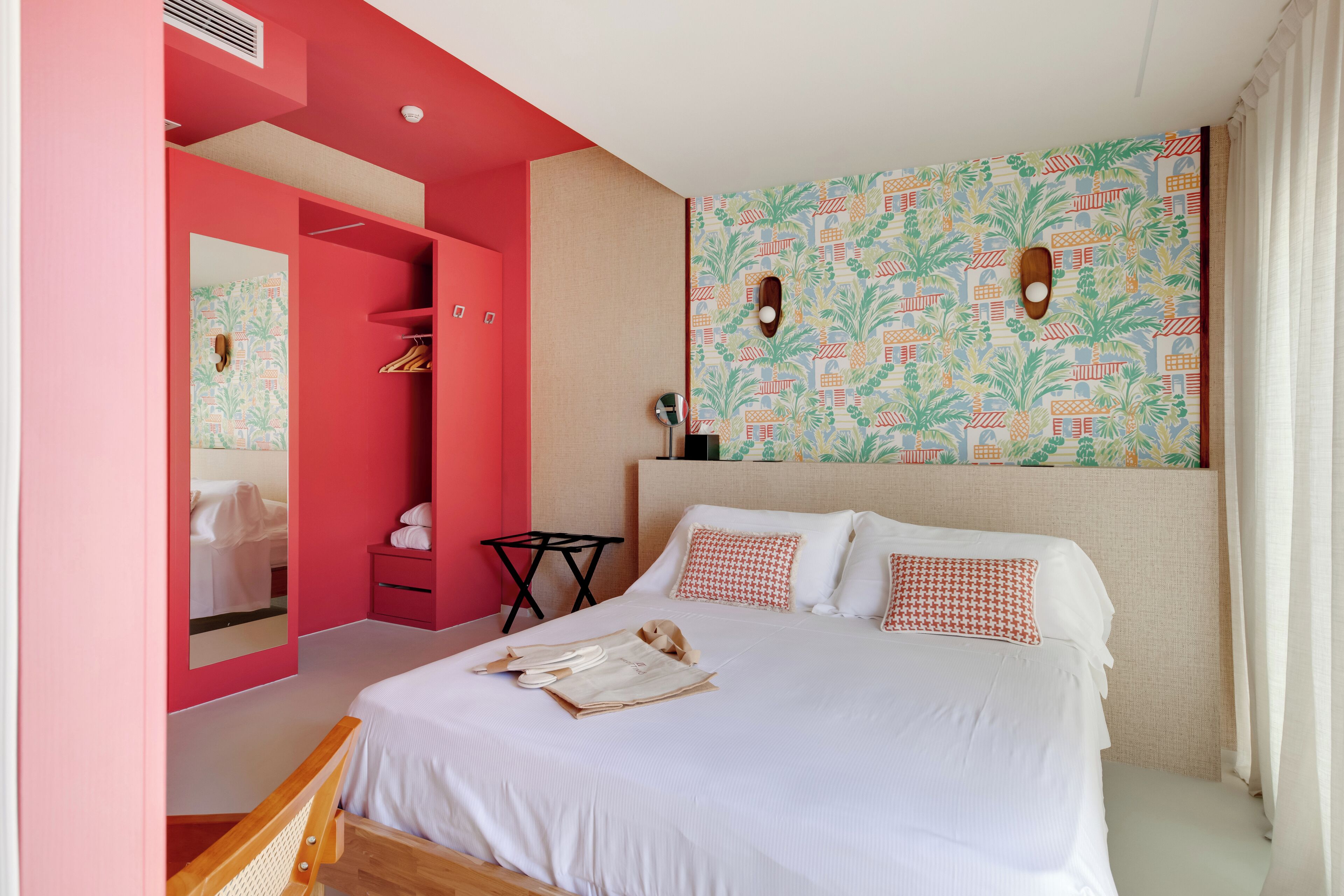 A bedroom with a large bed, a wardrobe, a mirror, and a patterned wall.