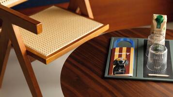 Una silla de madera con asiento tejido, una mesita con una bandeja que sostiene una botella de agua mineral, un vaso y un menú.