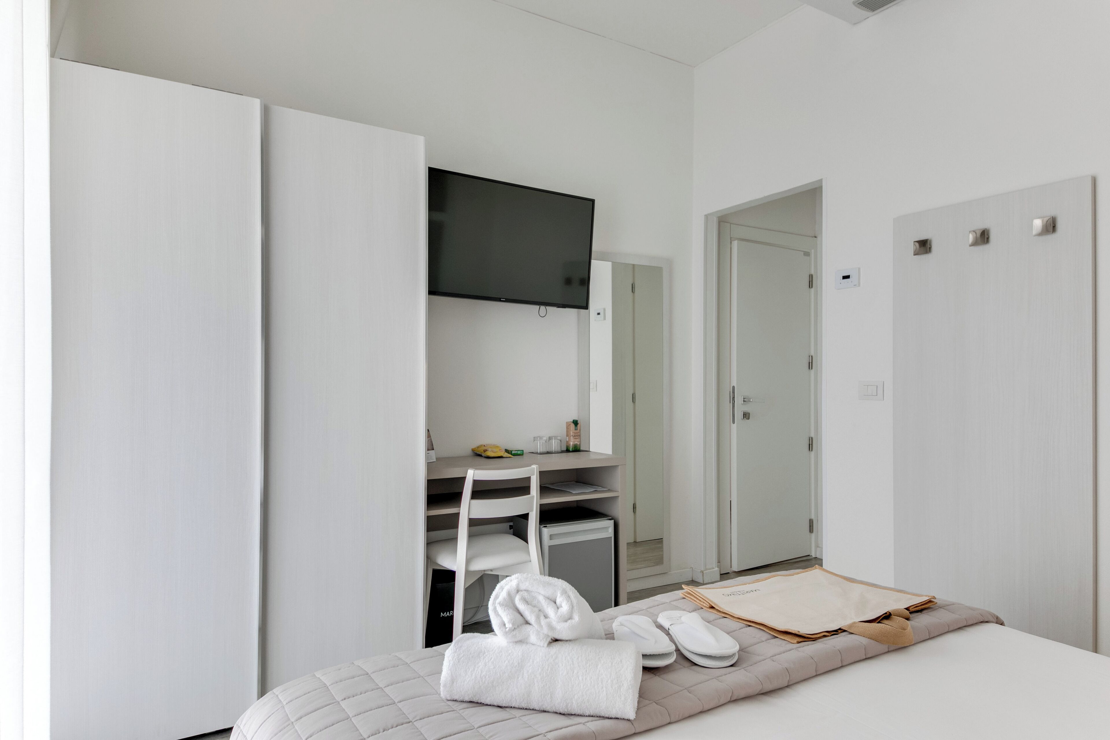 Een moderne hotelkamer met een bed, een flatscreen-tv boven een bureau en een kledingkast.