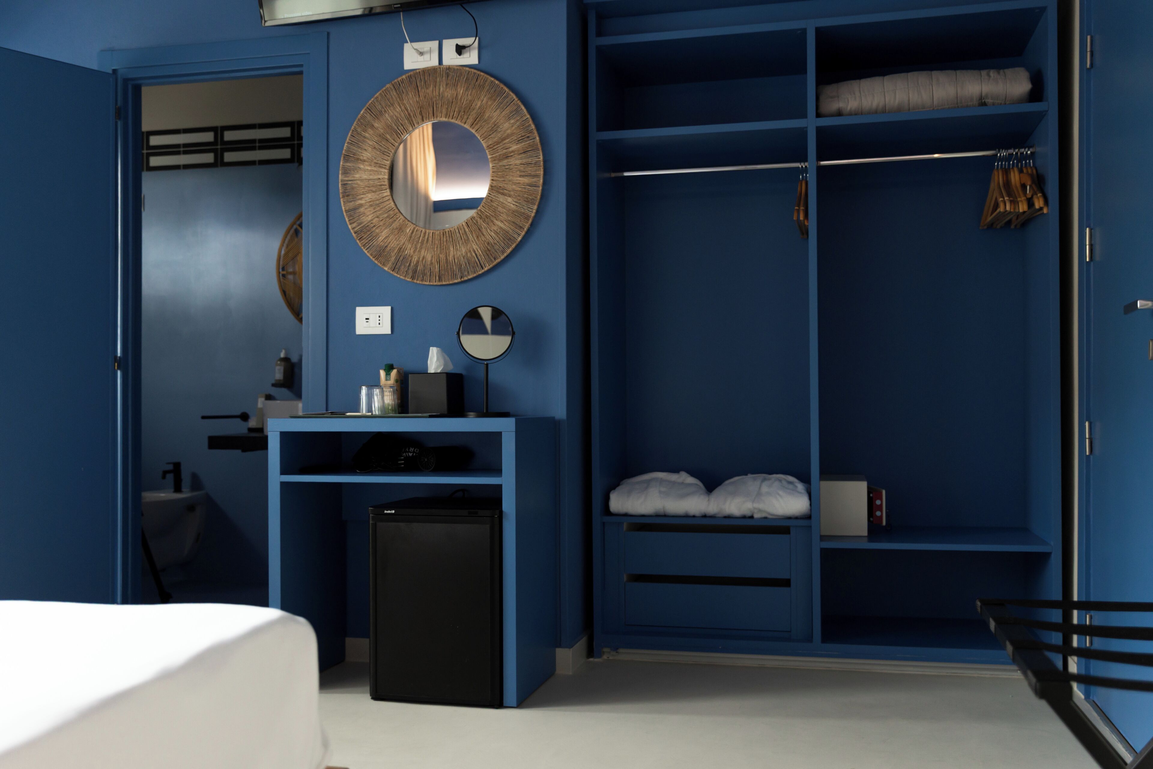 Una habitación con un armario azul, un espejo, un escritorio pequeño y una cama.