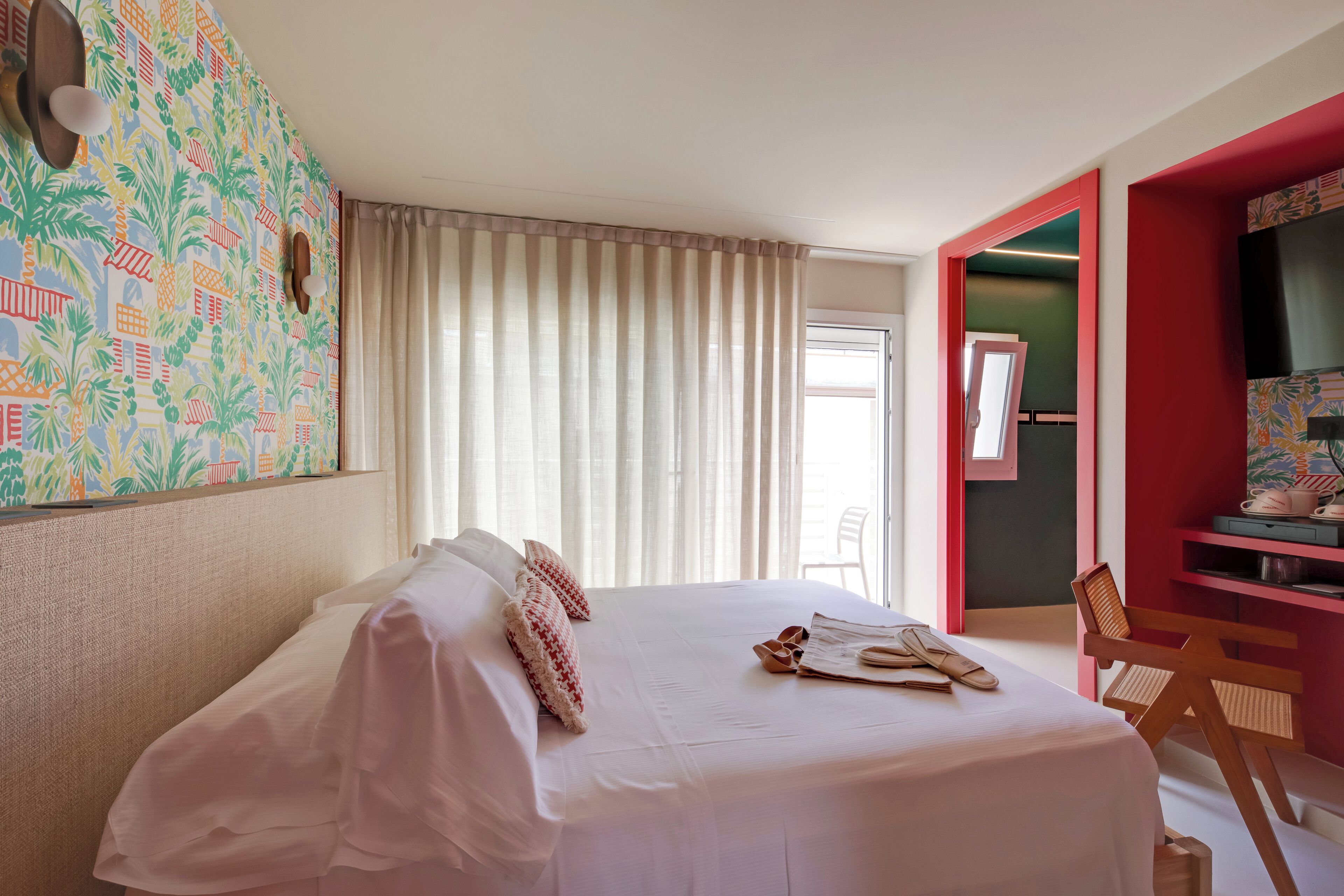 Habitación de hotel con cama, una silla, escritorio y pared colorida.
