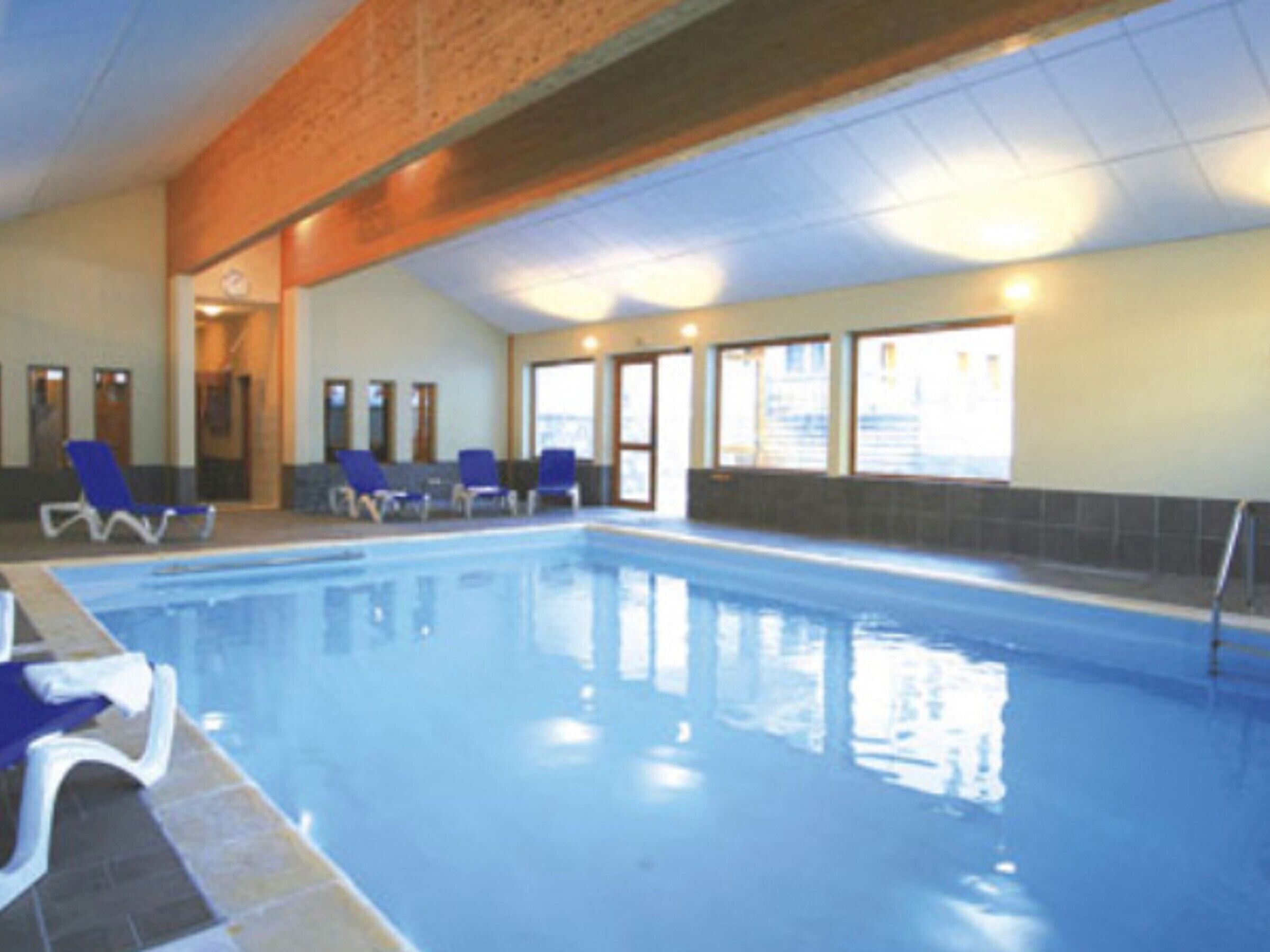 Une piscine intérieure à l’eau d’un bleu cristallin, entourée de chaises longues bleues.