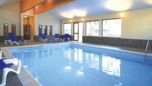 Una piscina interior con agua cristalina y azul, rodeada de sillas reclinables azules.