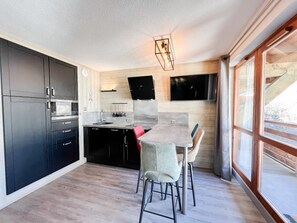 A modern kitchen with dark cabinets, a wooden countertop, and a dining area with a table and chairs. - Studio mezzanine 4 ppl 3* with WiFi, balcony, pool access (Valloire)