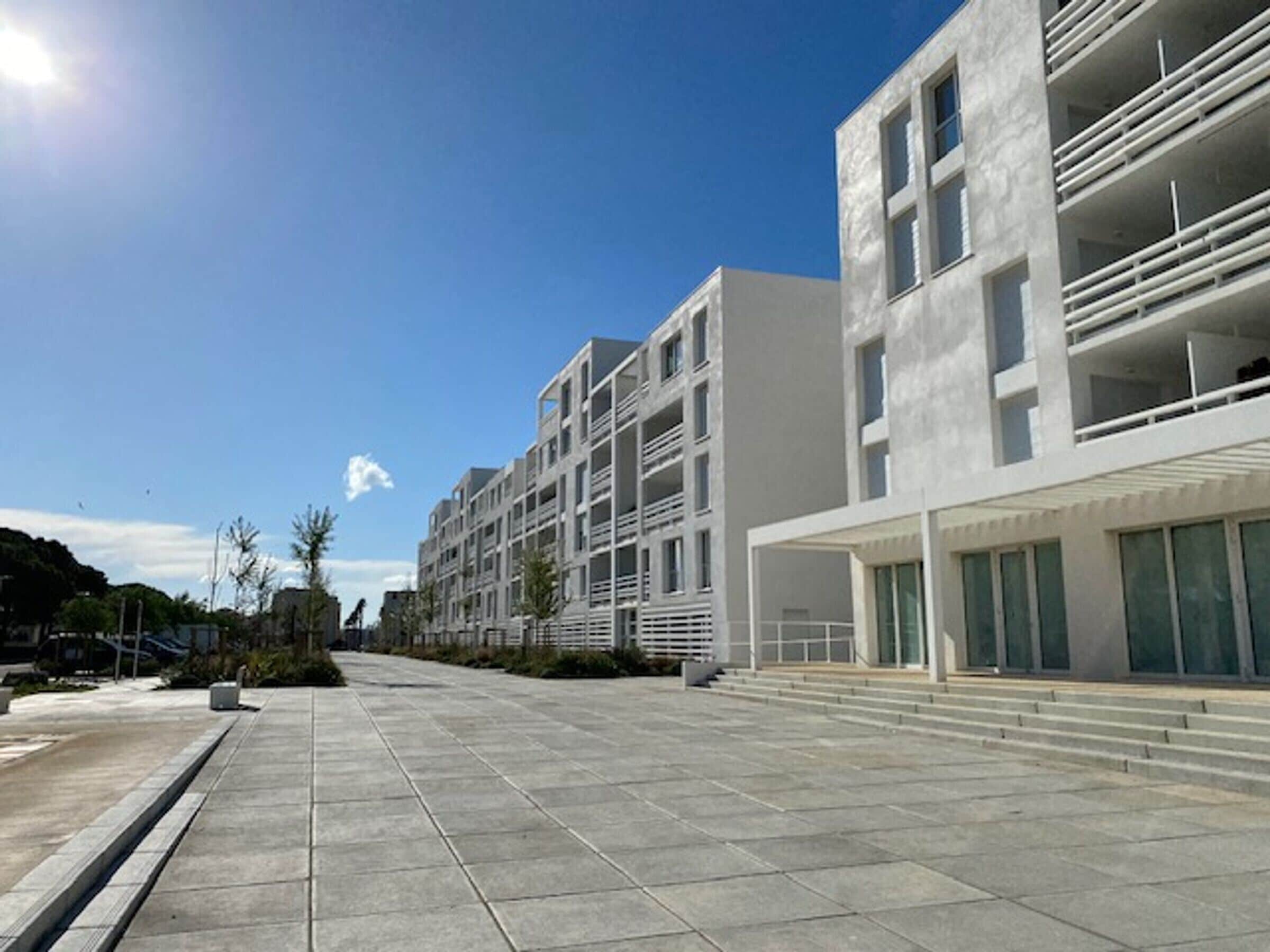 A modern building with multiple floors and balconies, a wide pedestrian area, and a clear sky.