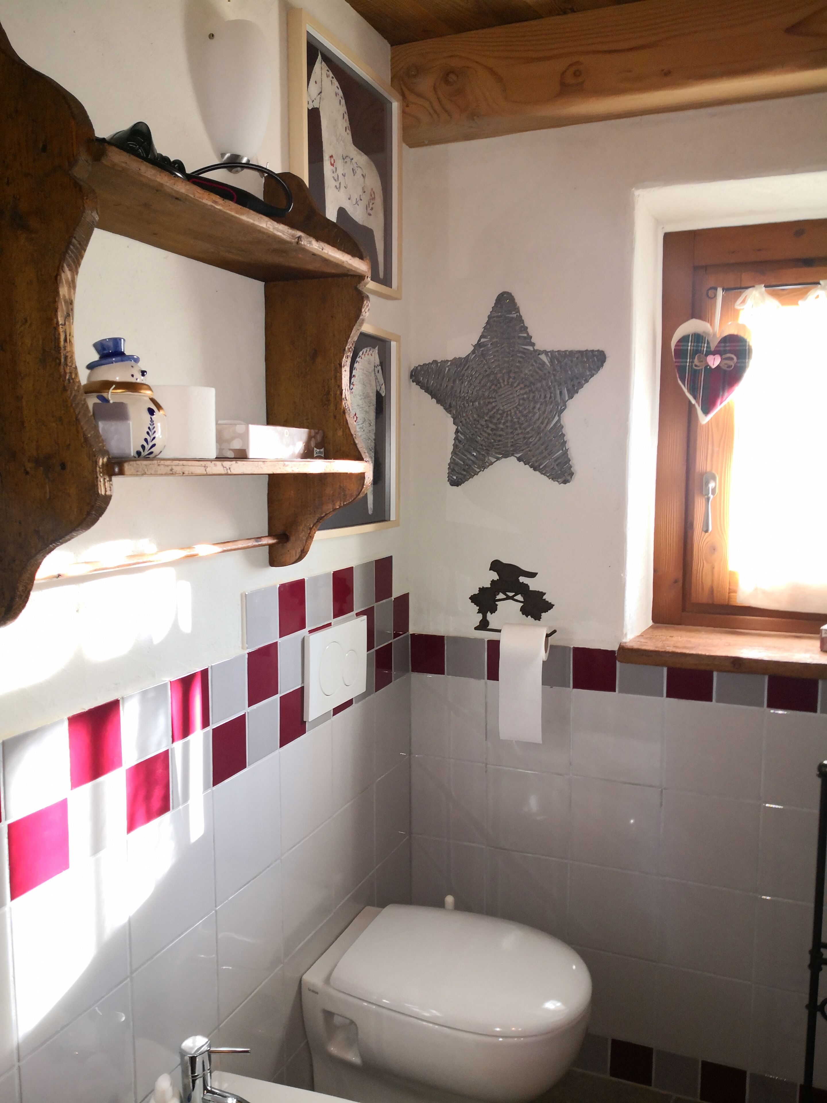 Une salle de bain avec des toilettes blanches, une décoration en forme d’étoile sur le mur, une décoration en forme de cœur sur la fenêtre et une étagère contenant divers objets.