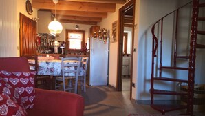 Une cuisine chaleureuse avec des poutres en bois, un coin repas avec un canapé rouge et un escalier menant à un autre niveau.