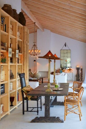 A dining area with a wooden table, chairs, and a chandelier. There is a bookshelf filled with books and decorative items. - Rufino Quinta (Alcantarilha)