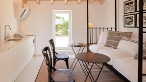Quarto moderno e minimalista com uma cama, uma mesinha, duas cadeiras, uma janela e ar condicionado fixado na parede.