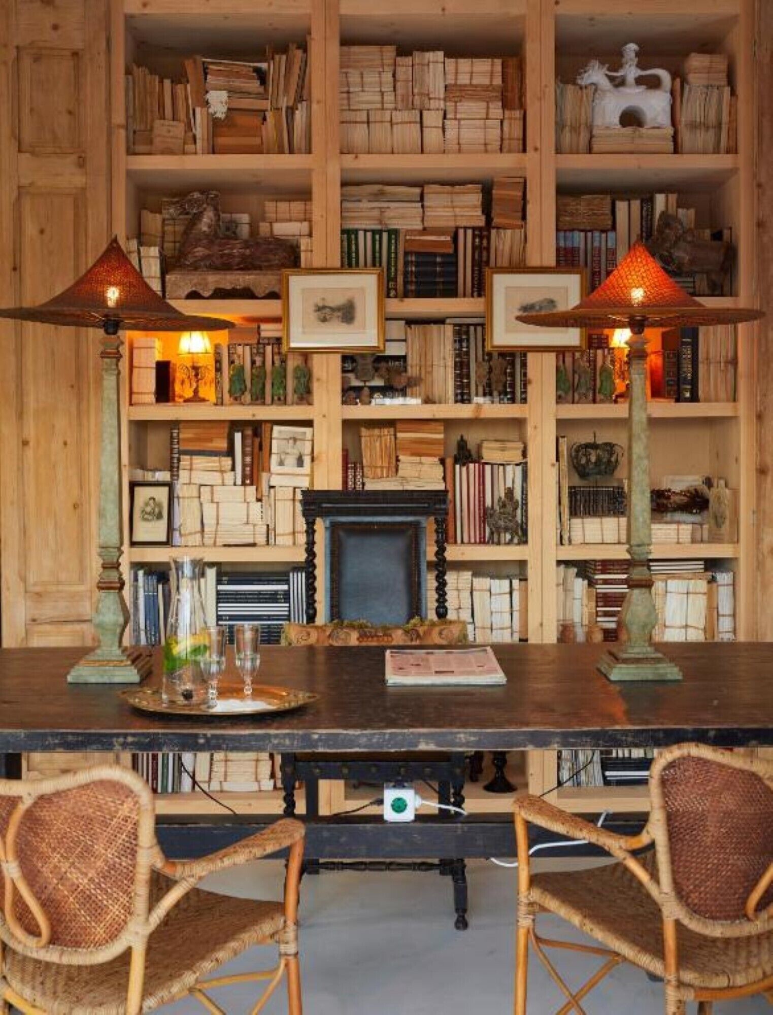 A wooden-paneled room with a large bookshelf, two lamps, and a fireplace.