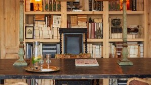 Um quarto com painéis de madeira, uma grande estante de livros, duas luminárias e uma lareira.