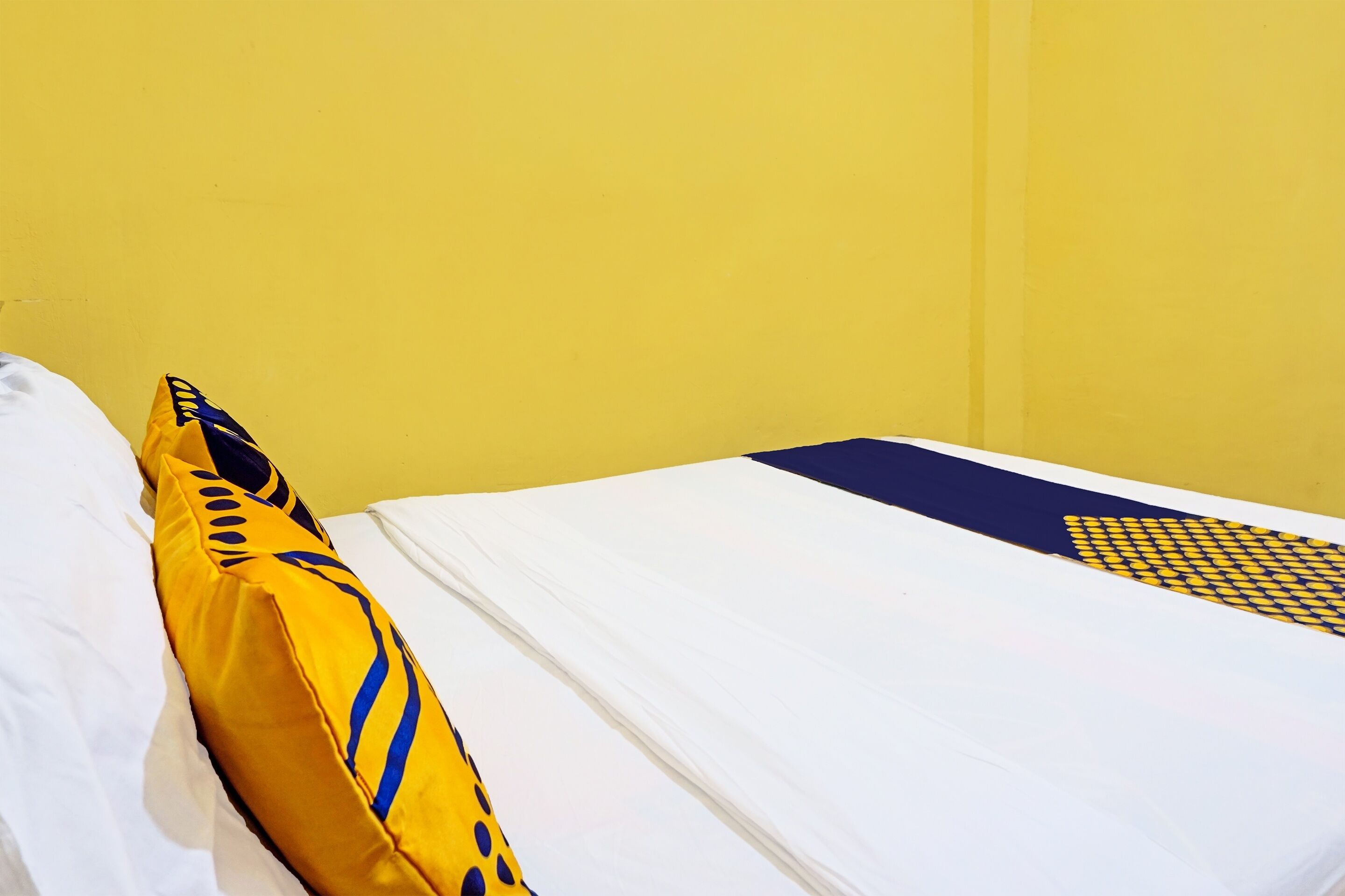 A bed with white sheets and a yellow pillow with blue patterns.