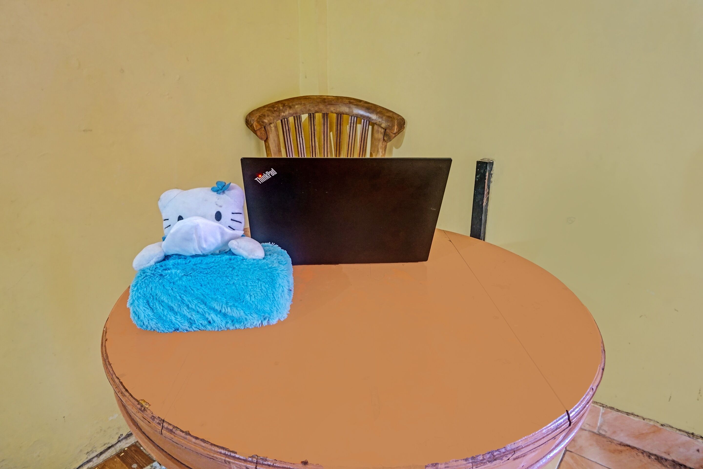 Uma mesa de madeira redonda com um laptop e um brinquedo de pelúcia em cima.