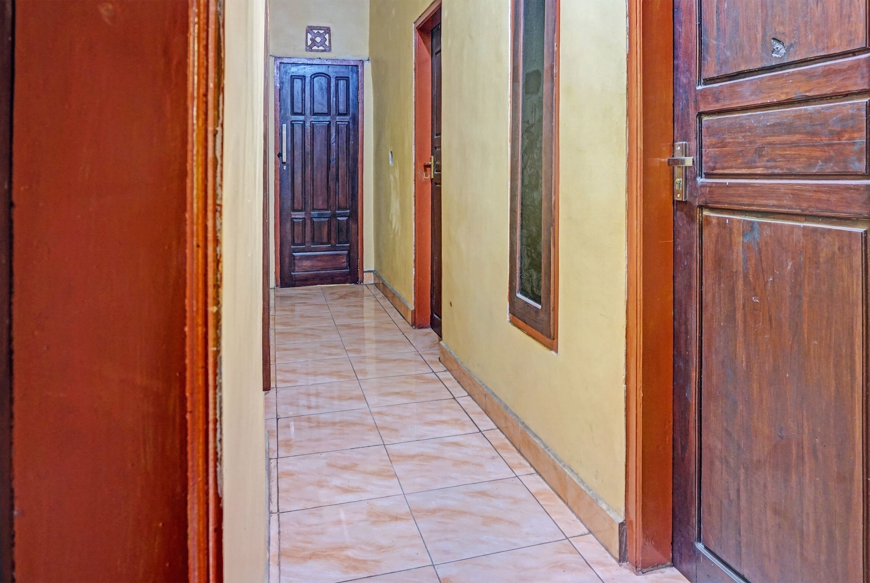 A hallway with tiled flooring, wooden doors, and a yellow wall.