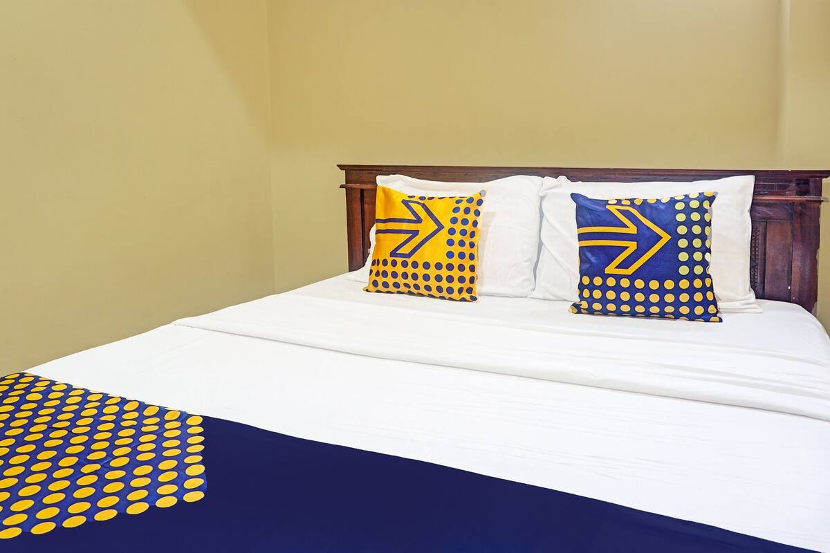 Un lit avec un drap blanc, deux oreillers à motifs jaunes et bleus, et une couverture bleue et jaune à pois.