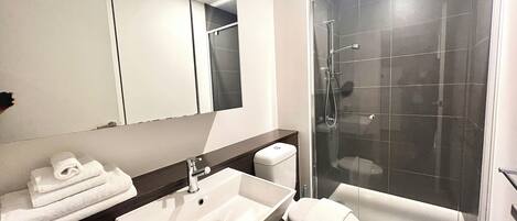 Un baño moderno con lavamanos, inodoro y ducha con mampara de vidrio.