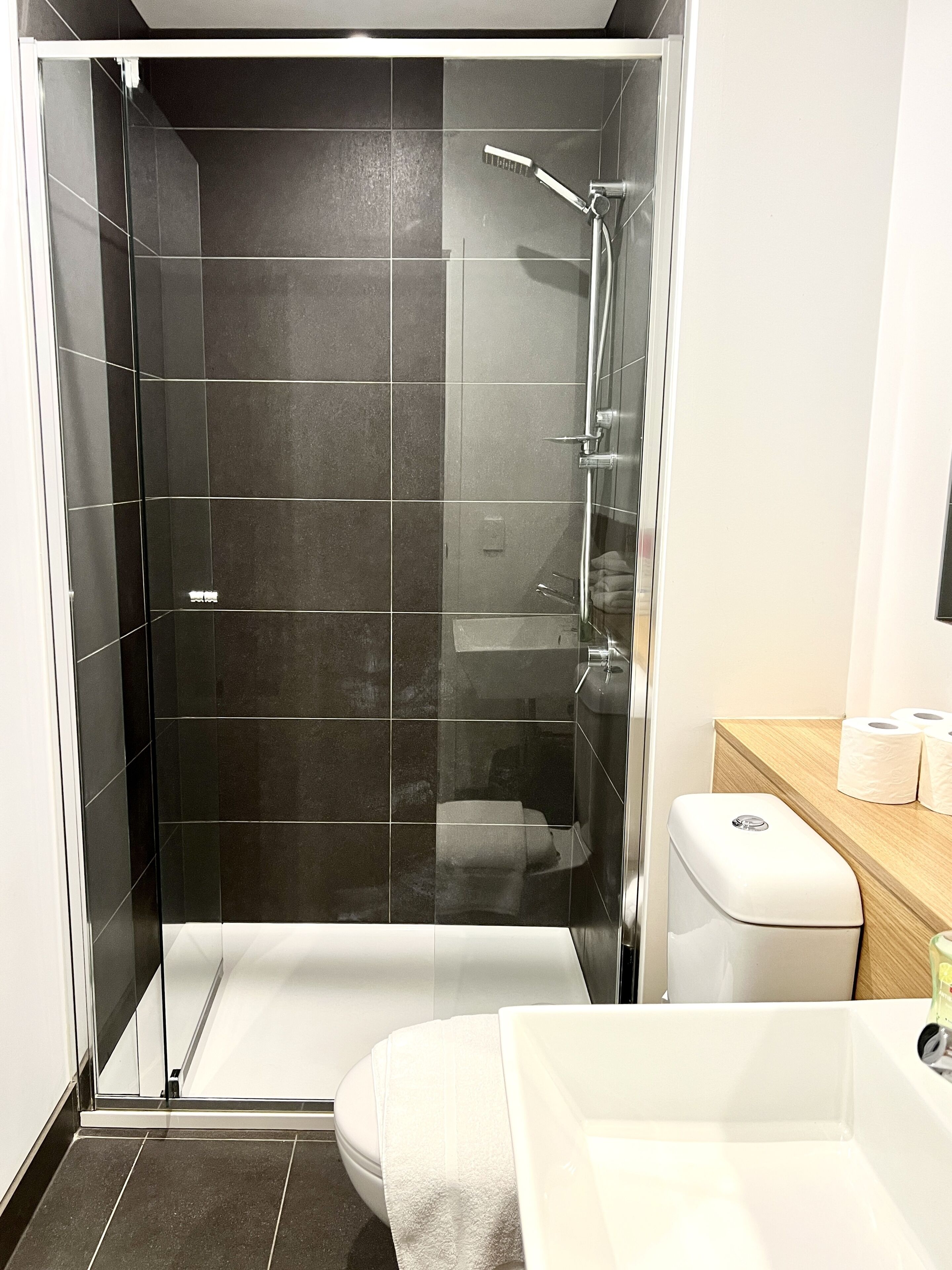 Un baño moderno con ducha de vidrio, bañera blanca y tocador de madera con artículos de aseo.
