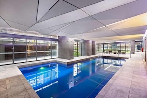An indoor swimming pool with clear glass walls, a tiled floor, and a modern ceiling design. - ReadySet Apartment at Midtown (Melbourne)