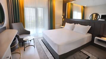 A modern hotel room with a large bed, a desk, a chair, a small table, and a large window with curtains.