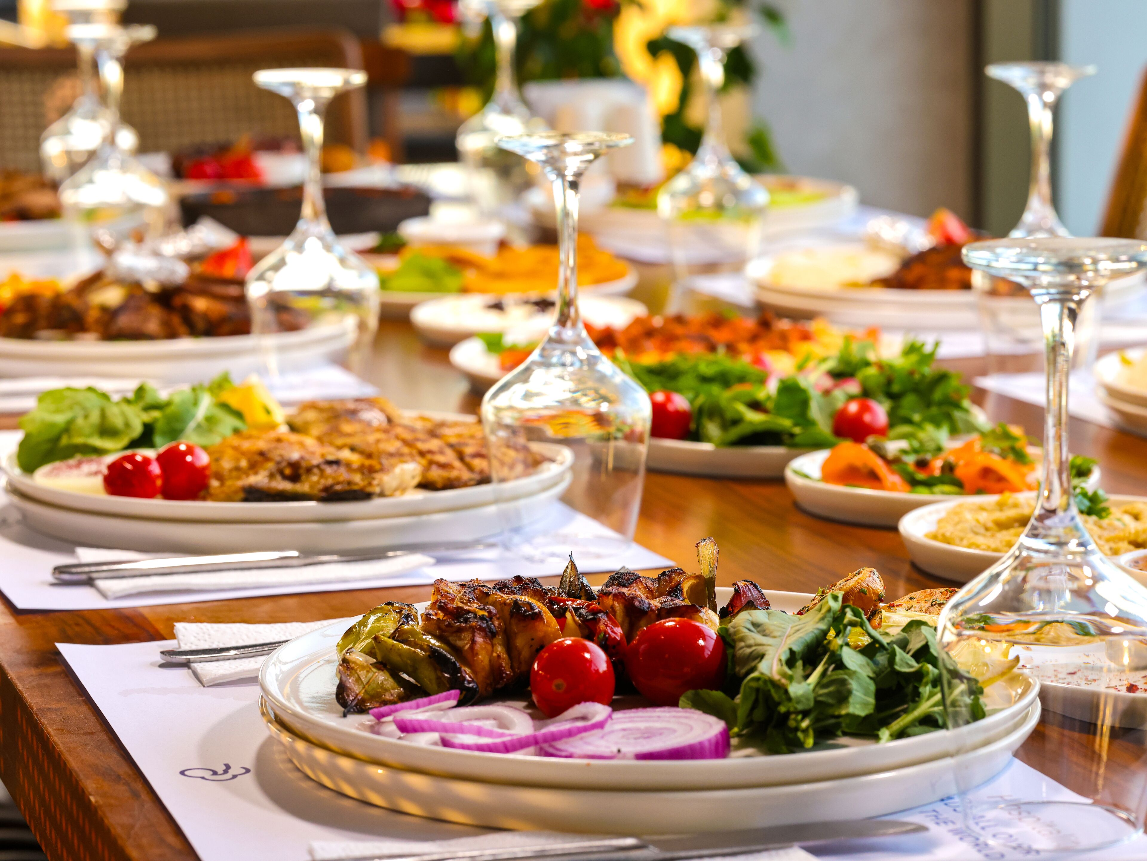 A dining table with various dishes, including grilled meat, salads, and vegetables, and multiple wine glasses.