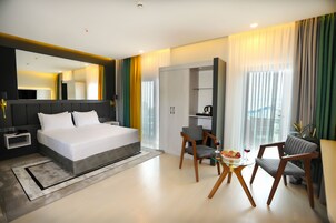 Una habitación de hotel moderna con una cama grande, un escritorio con silla, una mesa de comedor con sillas y un armario.