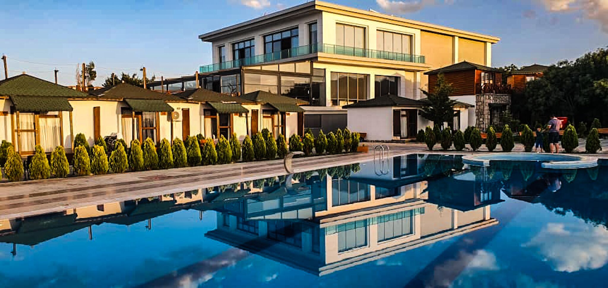 Un hotel moderno con piscina, varias habitaciones y un jardín bien cuidado.