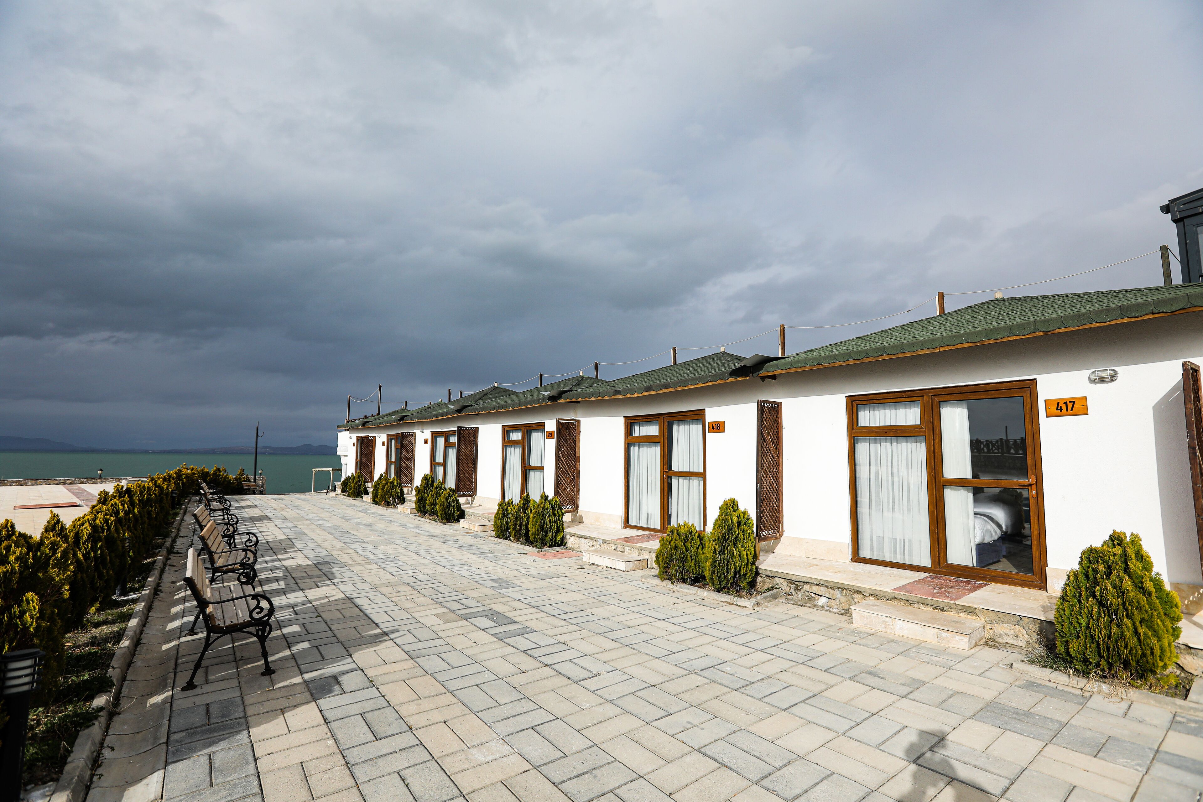 A row of white buildings with wooden doors and windows, a paved walkway, and a bench.