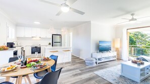 Enjoy a spacious living area with a large flat-screen TV, dining space, and balcony with a view of the surrounding greenery.