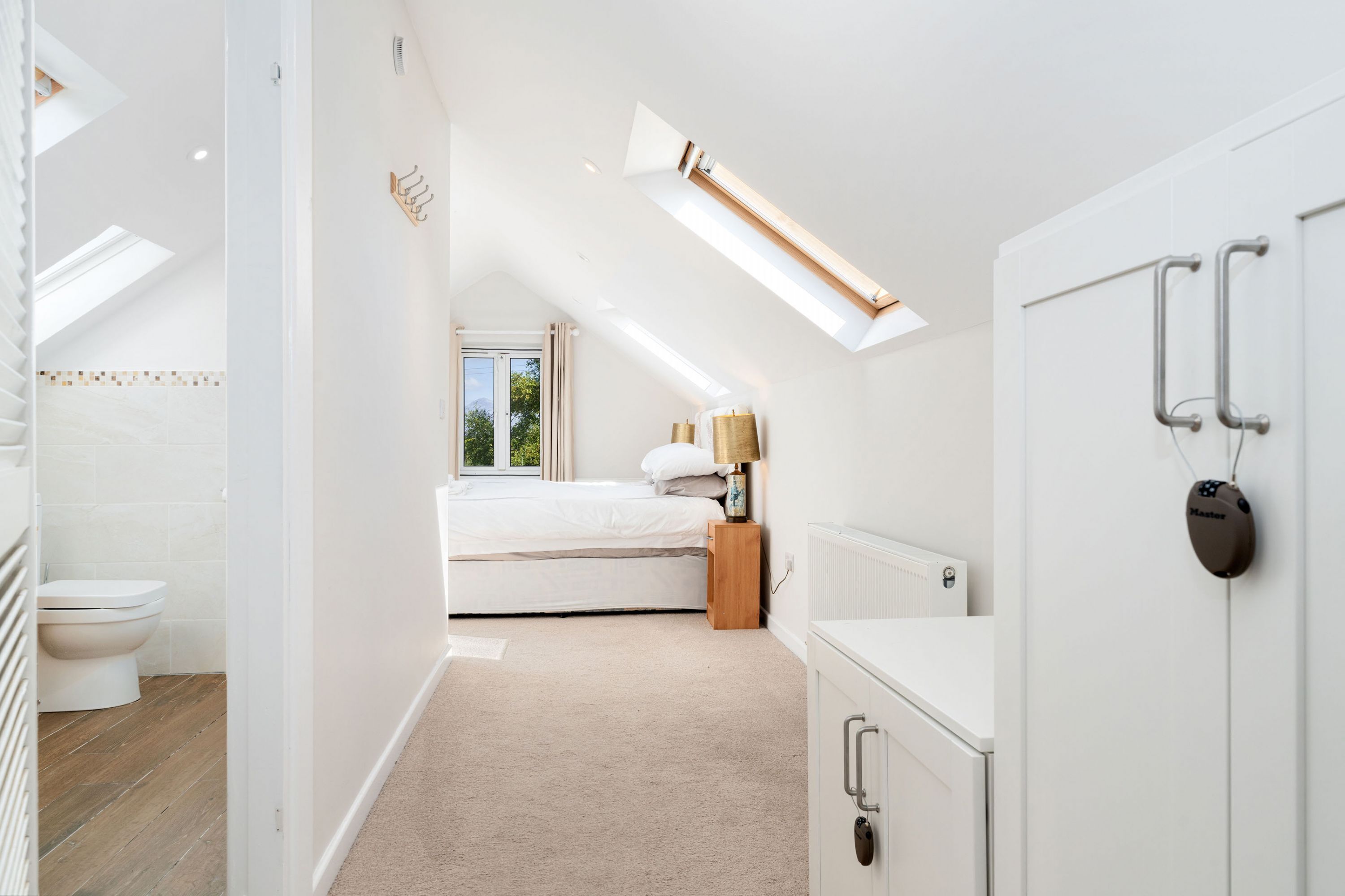 A bedroom with a skylight, a bed, a bedside table, a lamp, and a wardrobe.