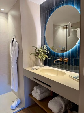 Une salle de bain moderne avec un grand miroir, un lavabo beige et un peignoir blanc suspendu à un porte-serviettes.