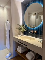 Un baño moderno con un espejo grande, un lavabo color beige y una bata blanca colgada en un perchero.