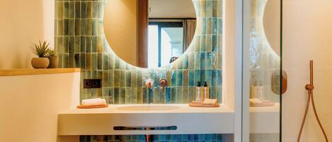 A bathroom with a round mirror, a sink, a toilet, and a glass-enclosed shower.