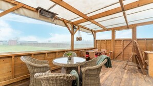 A covered outdoor area with wooden walls and a glass roof, featuring wicker furniture and a table with chairs. - Comfortable Holiday Home With Garden (Hellendoorn)