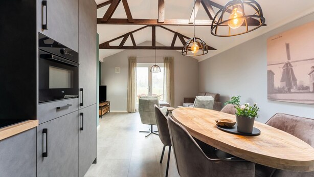 A modern kitchen with a built-in oven and a dining area with a wooden table and chairs. - Comfortable Holiday Home With Garden (Hellendoorn)