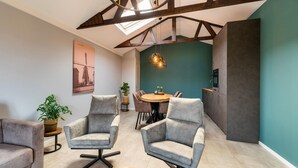 A modern living room with a high ceiling, exposed beams, a round dining table, and two grey armchairs. - Comfortable Holiday Home With Garden (Hellendoorn)