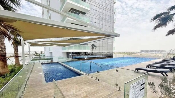A modern building with a rooftop pool, glass railings, and palm trees.