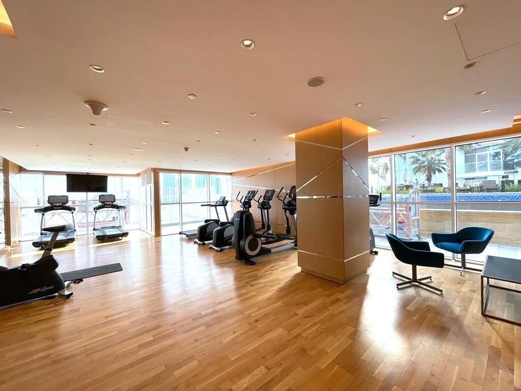 A modern gym with exercise equipment, large windows, and a wooden floor.
