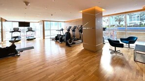 A modern gym with exercise equipment, large windows, and a wooden floor.