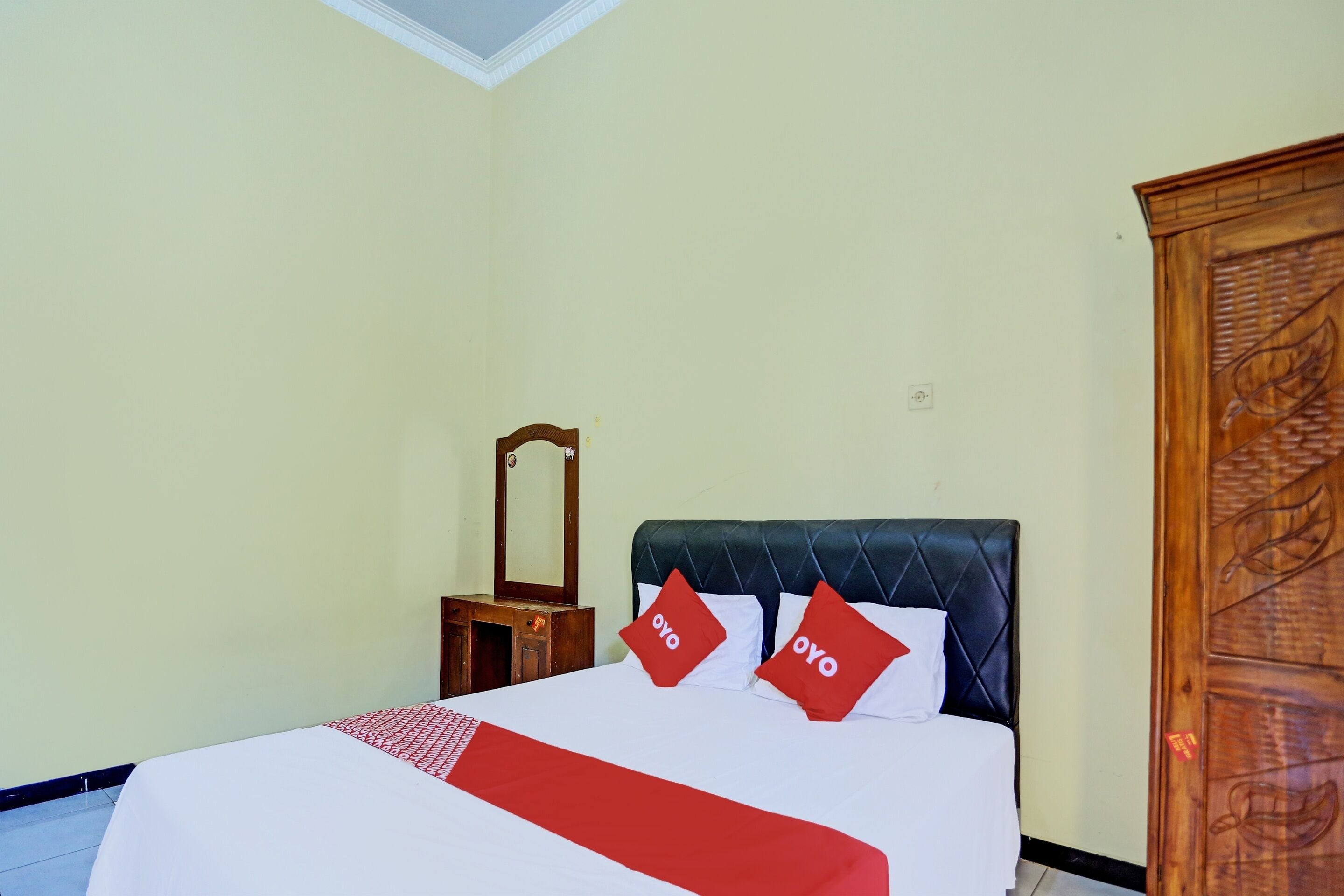 A hotel room with a bed, a wooden nightstand, a mirror, and a wardrobe.