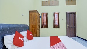 A hotel room with a bed, two pillows, a wooden wardrobe, a window with curtains, and a door.