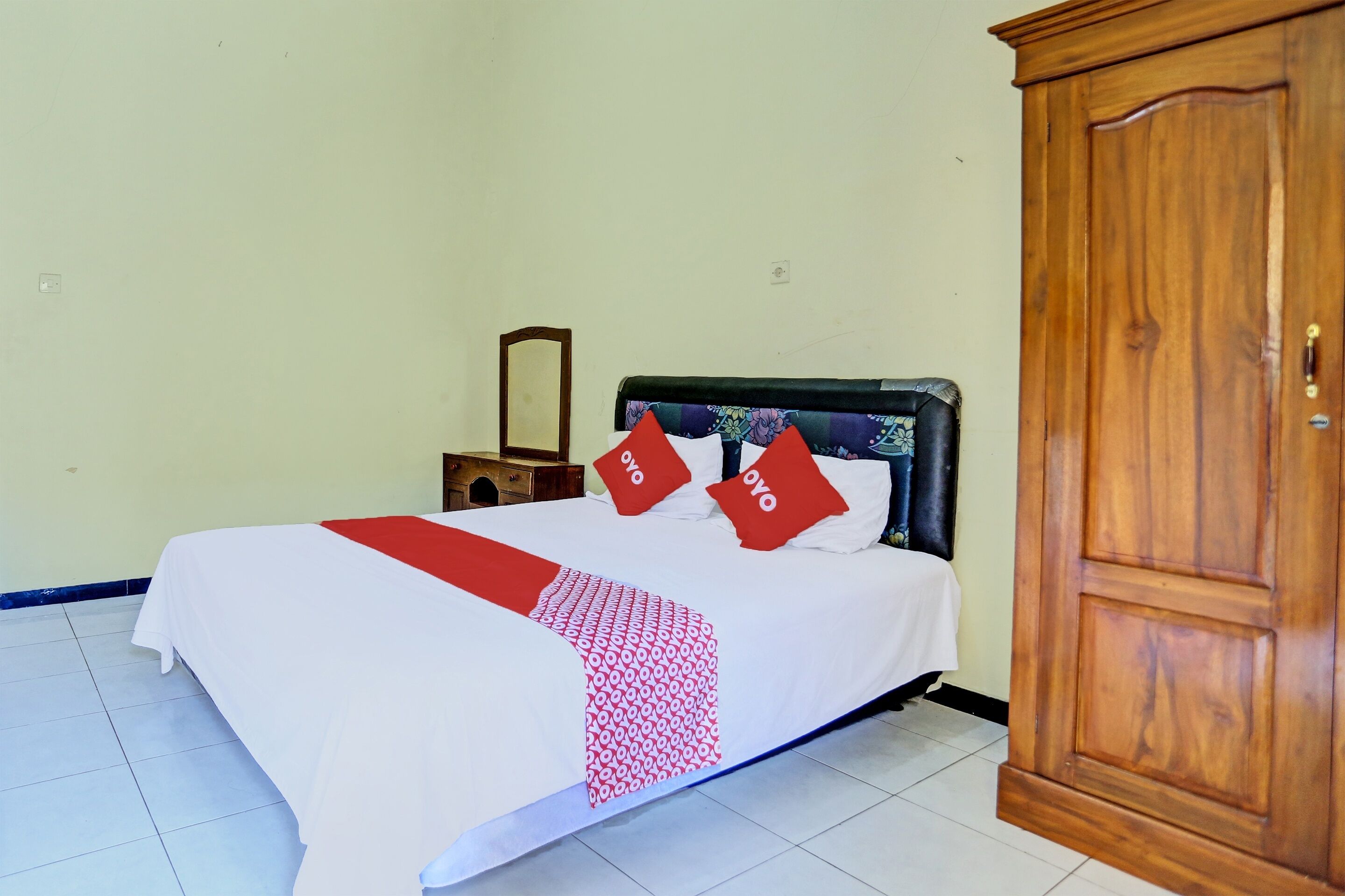 A neatly made bed with a white and red bedspread, two red pillows, and a wooden headboard.