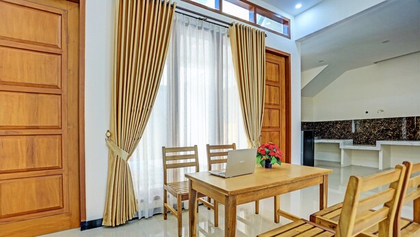 A dining area with a wooden table and chairs, a laptop, and a vase with flowers.