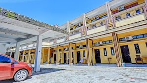 A multi-story building with a covered parking area and a red car parked in front.