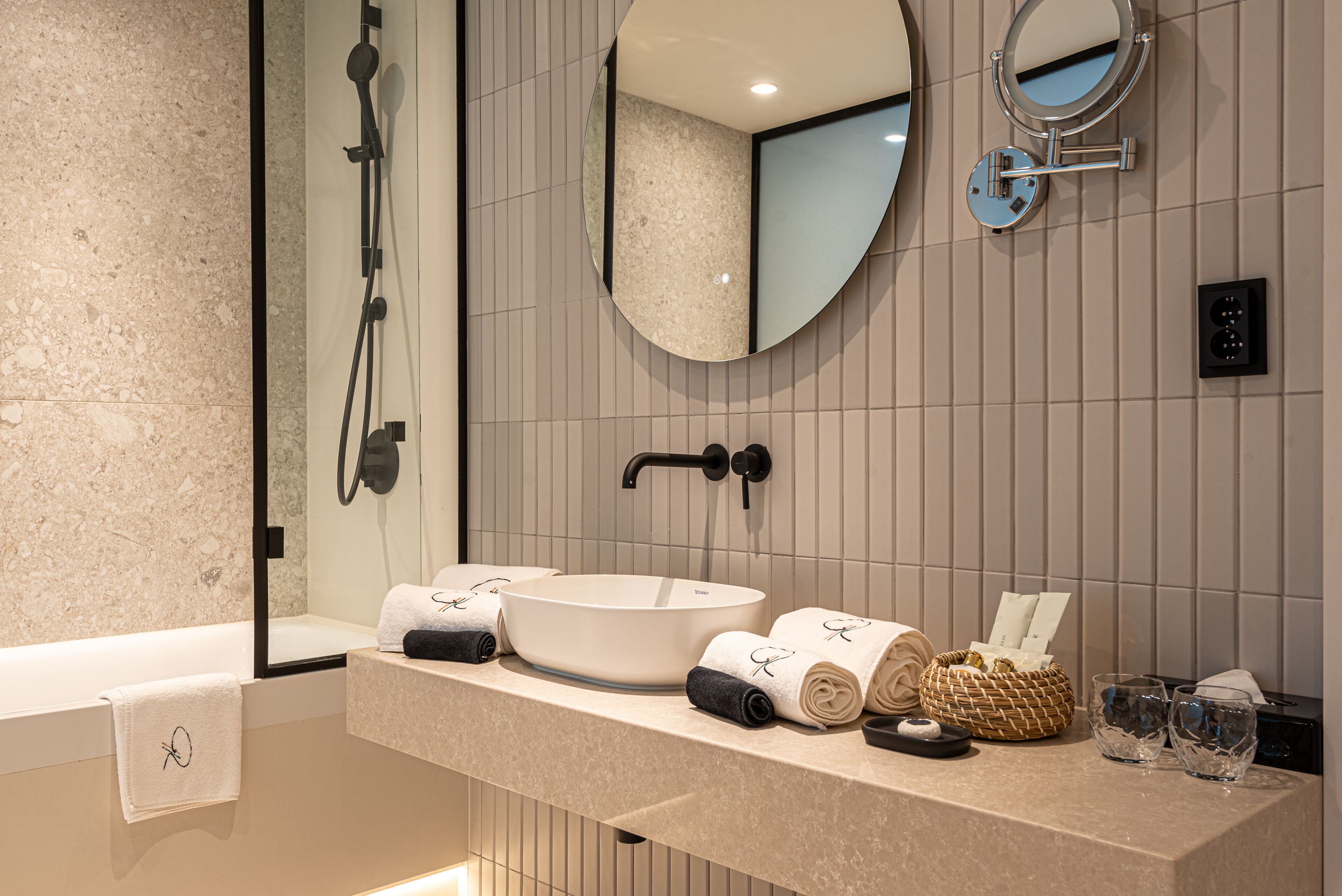 Een moderne badkamer met een groot ovaal wastafel, een handdouche, een spiegel, en netjes opgevouwen handdoeken en toiletartikelen.