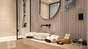 Een moderne badkamer met een groot ovaal wastafel, een handdouche, een spiegel, en netjes opgevouwen handdoeken en toiletartikelen.