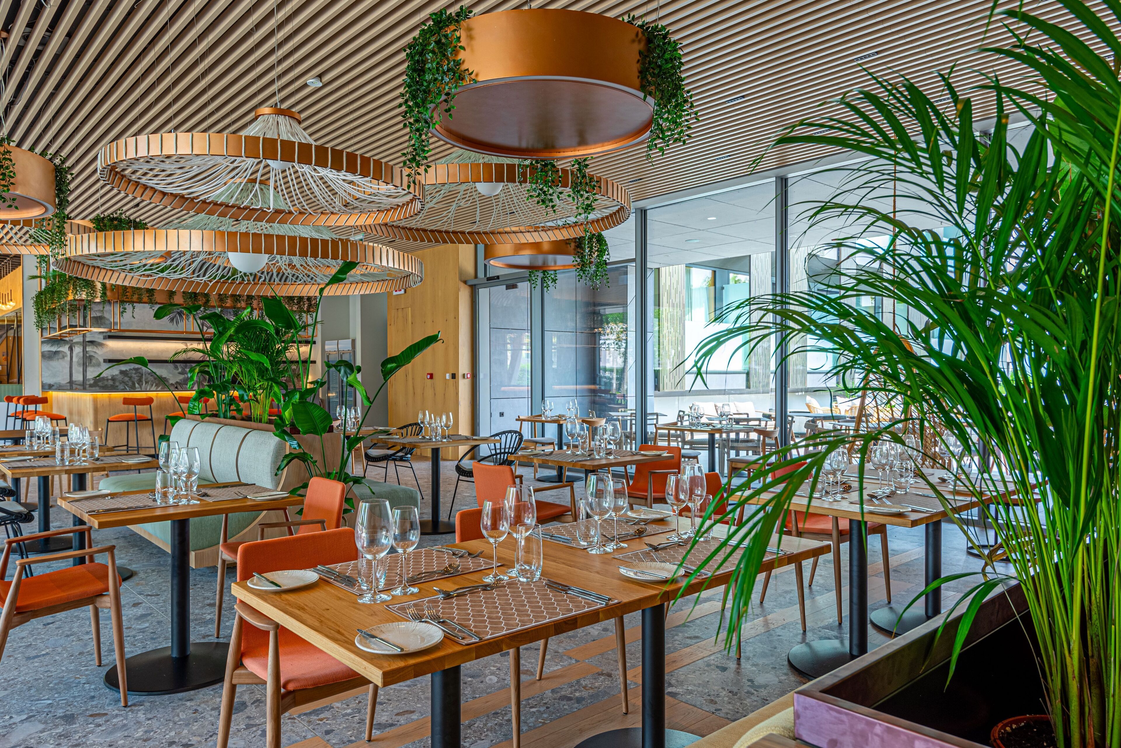A modern restaurant with wooden tables, orange chairs, and hanging plants.