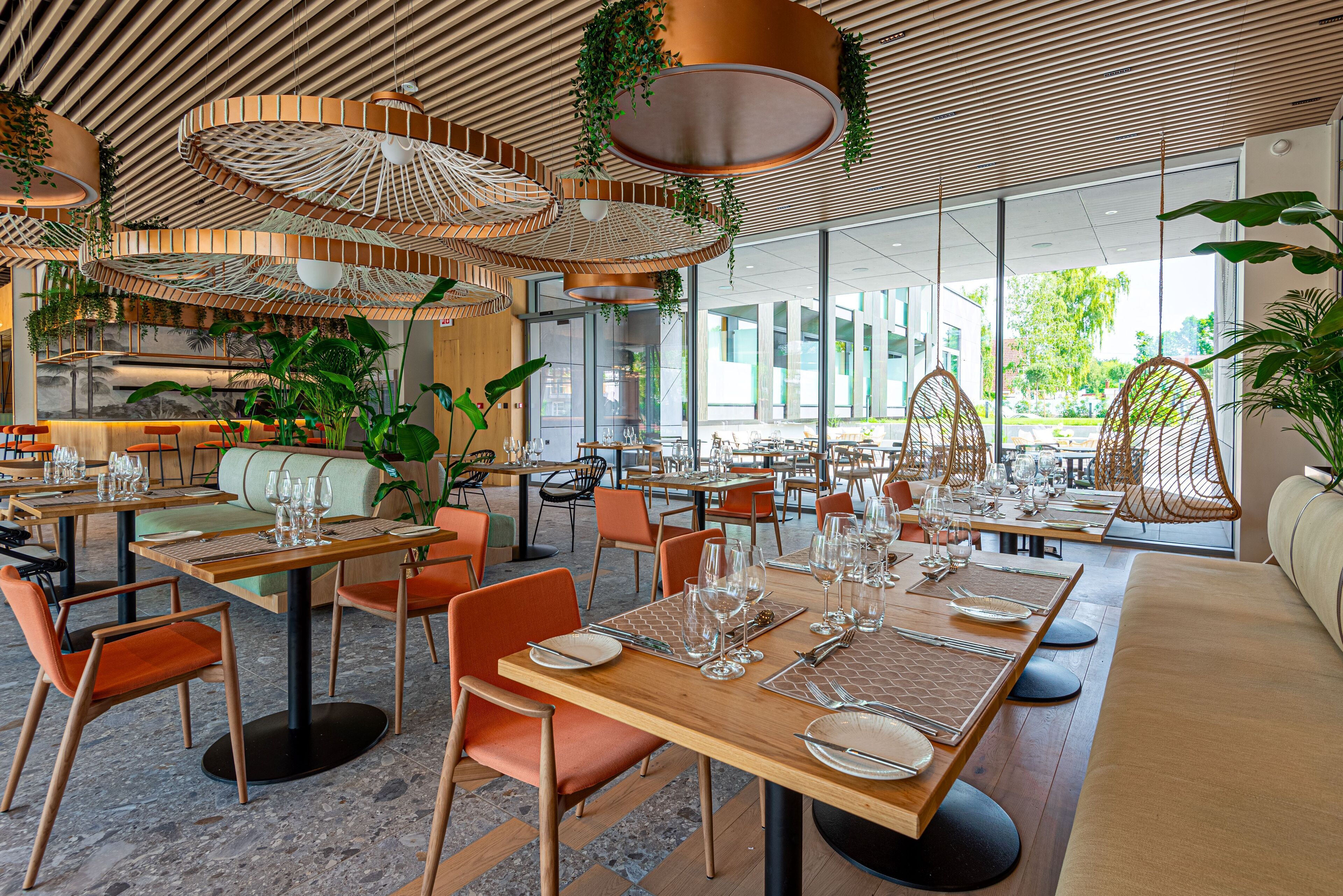 A modern restaurant interior with wooden tables, orange chairs, and hanging wicker lamps.