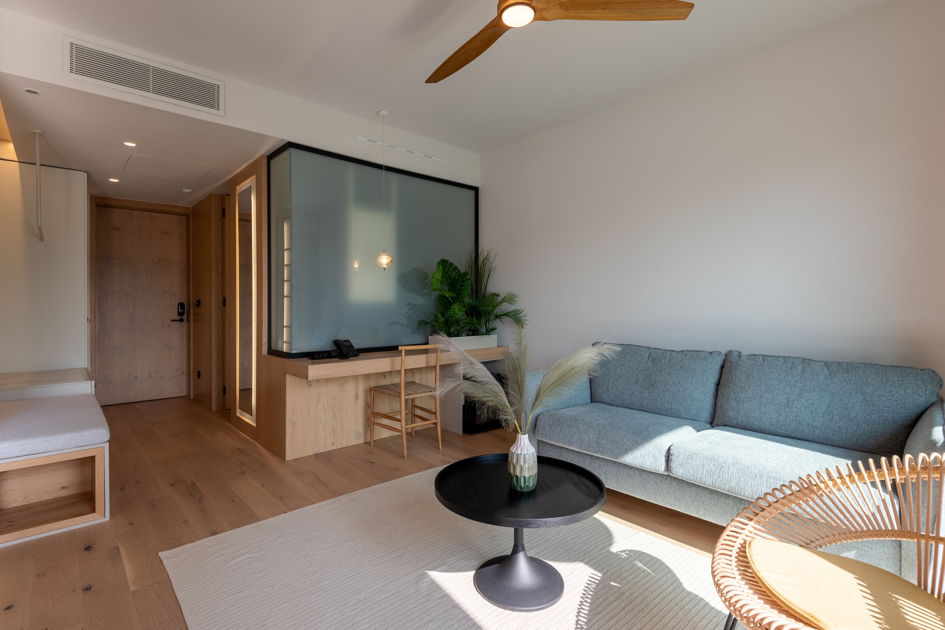 A modern living room with a sofa, a round table with a vase, a wooden bench, and a ceiling fan.