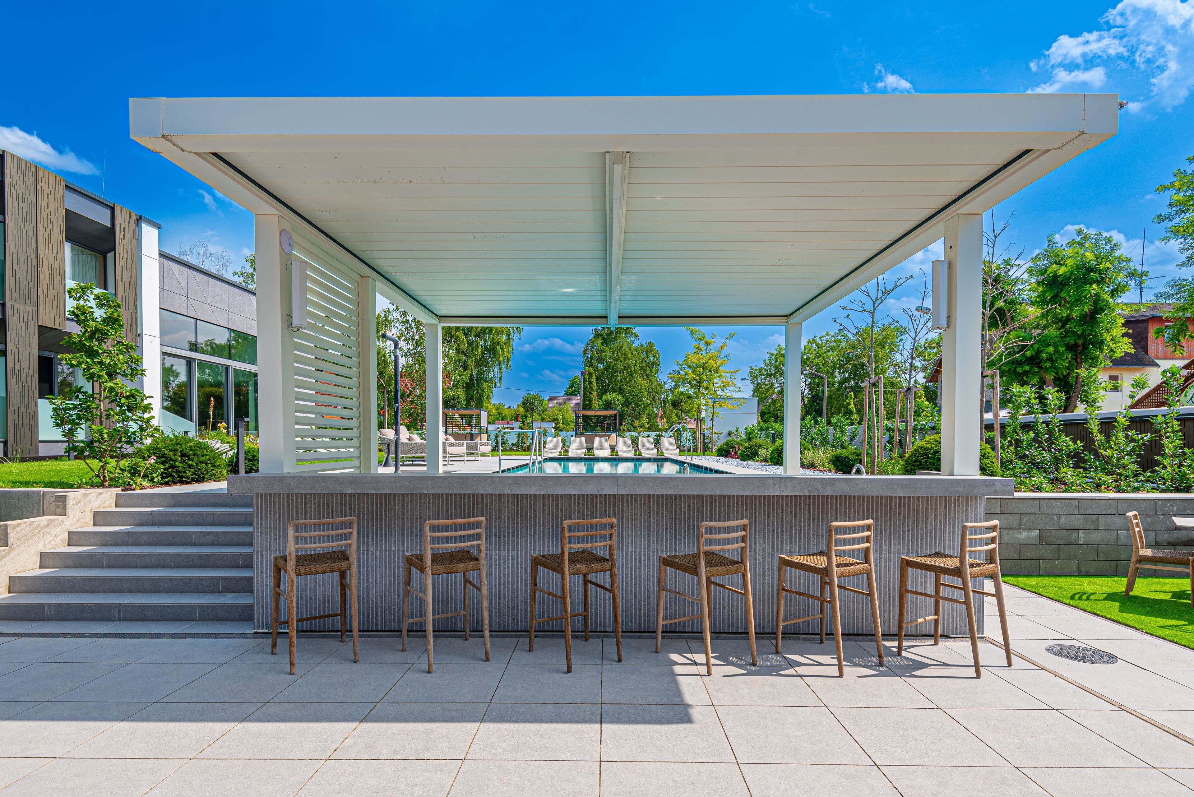 Un área de bar al aire libre con vista a la piscina, rodeada de escalones y follaje.