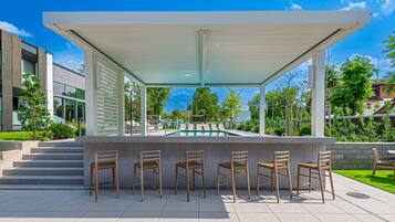 Un área de bar al aire libre con vista a la piscina, rodeada de escalones y follaje.